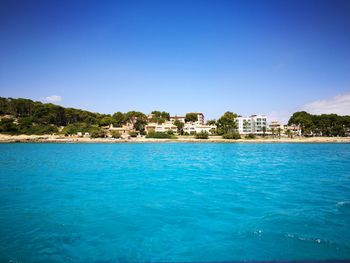 Scenic view of sea by buildings against clear blue sky