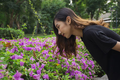 Side view of young woman looking at pink flowers in park
