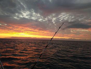 Fishing rod over sea against sky during sunset