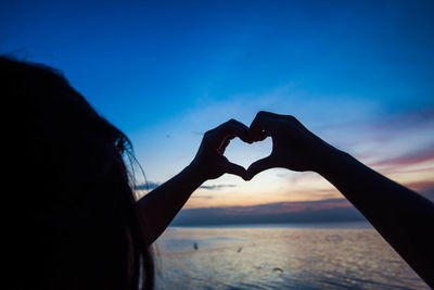 Silhouette woman making heart shape at beach against blue sky during sunset