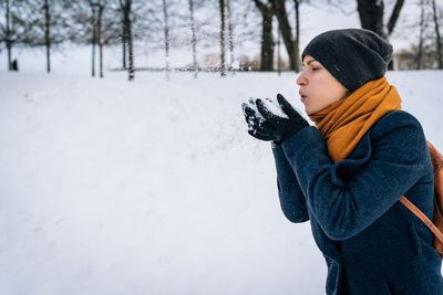 A young woman blows on the snow in her palms