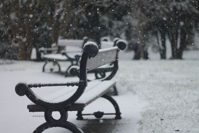 Empty bench in park during snowfall