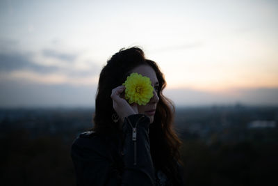 Portrait of man holding flower against sky during sunset