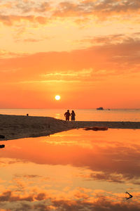 Silhouette people on sea against sky during sunset