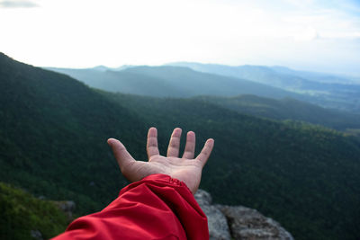 Cropped hand of person by mountain against sky