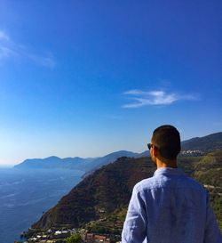 Rear view of man standing on mountain against blue sky