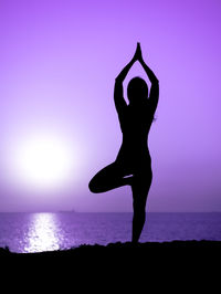 Silhouette woman standing on purple sea against sky