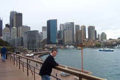 Woman standing on railing by river against cityscape