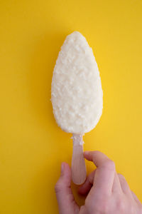 Cropped hand holding ice cream cone against yellow background