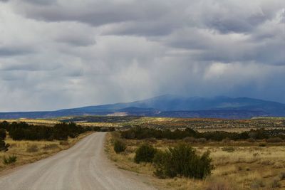 Road passing through field against cloudy sky