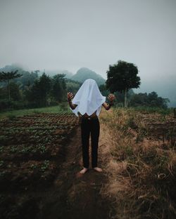 Rear view of man standing on field against sky