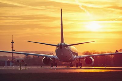 Airplane flying at airport runway against sky during sunset