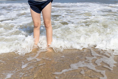 A boy stands on the sandy beach and enjoys the waves on his legs.