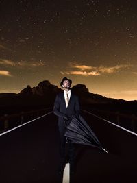 Mature man with umbrella standing on road against star field