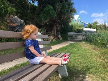 Full length of cute girl sitting on bench against trees