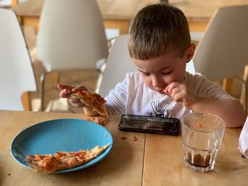 Boy using mobile phone while eating food on table