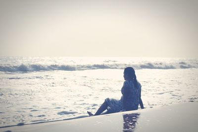 Man sitting on snow covered shore against sky