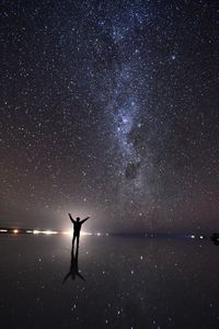 Silhouette person standing in sea against sky at night