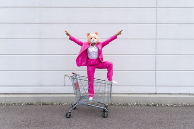 Full length of girl with pink umbrella against wall