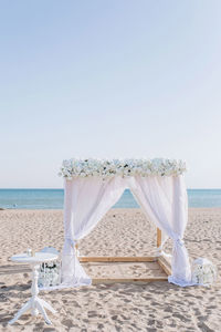 White wedding altar made of fabric and white roses against the background of sea sand and water