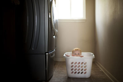 Portrait of cute baby boy in laundry basket by washing machine