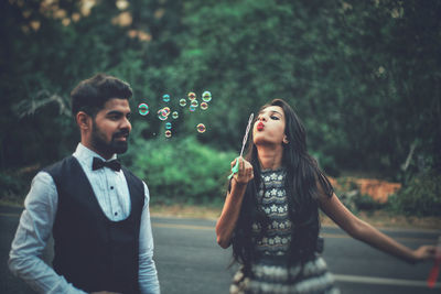 Boyfriend looking at girlfriend blowing bubbles on road
