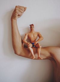 Midsection of shirtless woman flexing muscle with toy against wall