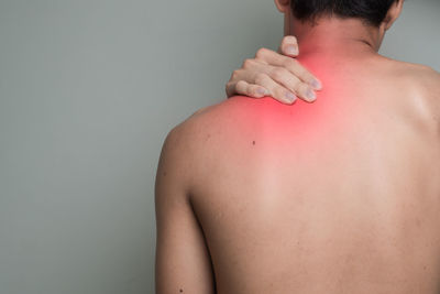 Rear view of shirtless man with shoulder pain against gray background