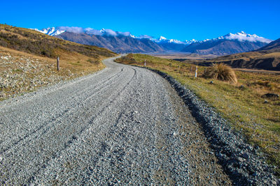 Road leading towards mountains against blue sky