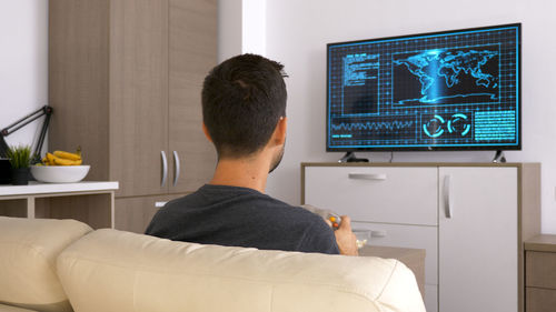 Rear view of man using laptop at home