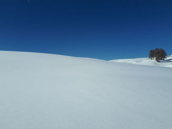 Snow covered land against clear blue sky