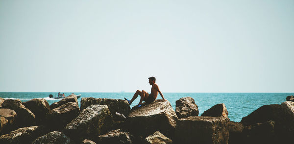 People standing on rock by sea against clear sky