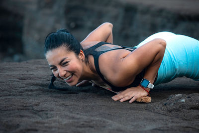 Side view of sporty female balancing in plank position during intense training on rocky seashore in summer