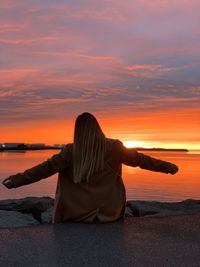Rear view of woman standing at beach against sky during sunset / midnight sun