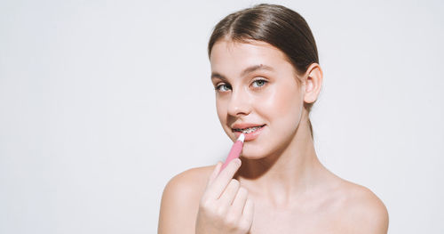 Beauty portrait of young girl with fresh skin, teenager doing lips makeup on white background 
