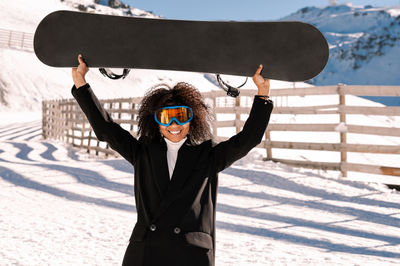 African american woman with goggles and a snowboard on a snowy mountain during winter