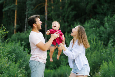 Happy young parents with a baby are walking through the forest, having fun and enjoy