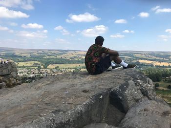 Side view of man sitting on cliff against sky