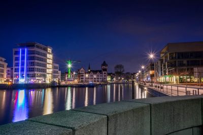 Illuminated buildings by river against sky at night