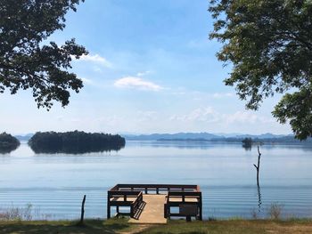 Empty bench by lake against sky