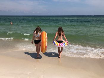 Rear view of girls wearing bikinis walking at beach against sky