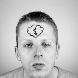 Close-up of young man with drawing on forehead against white background