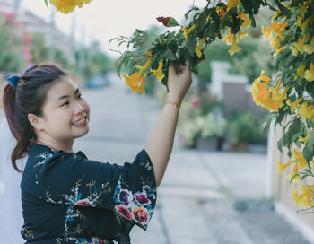 Side view of smiling young woman touching yellow flowers