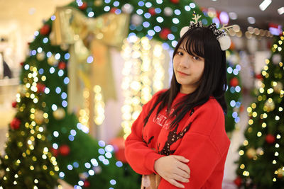 Young woman standing against illuminated christmas tree