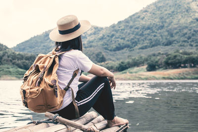 Rear view of woman sitting by lake on wooden raft