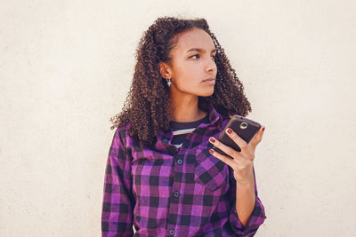 Beautiful young woman using mobile phone against wall