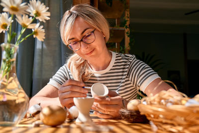 Blond woman preparing easter decoration at home, painting colorful easter eggs and coloring egg cups