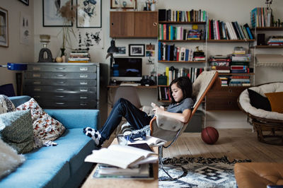 Full length of boy using smart phone while sitting in living room at home