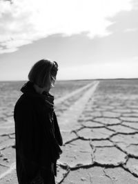 Side view of woman standing on salt flat against sky during sunny day