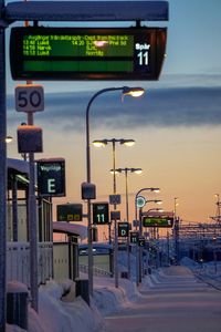 Illuminated street light by sea against sky during sunset